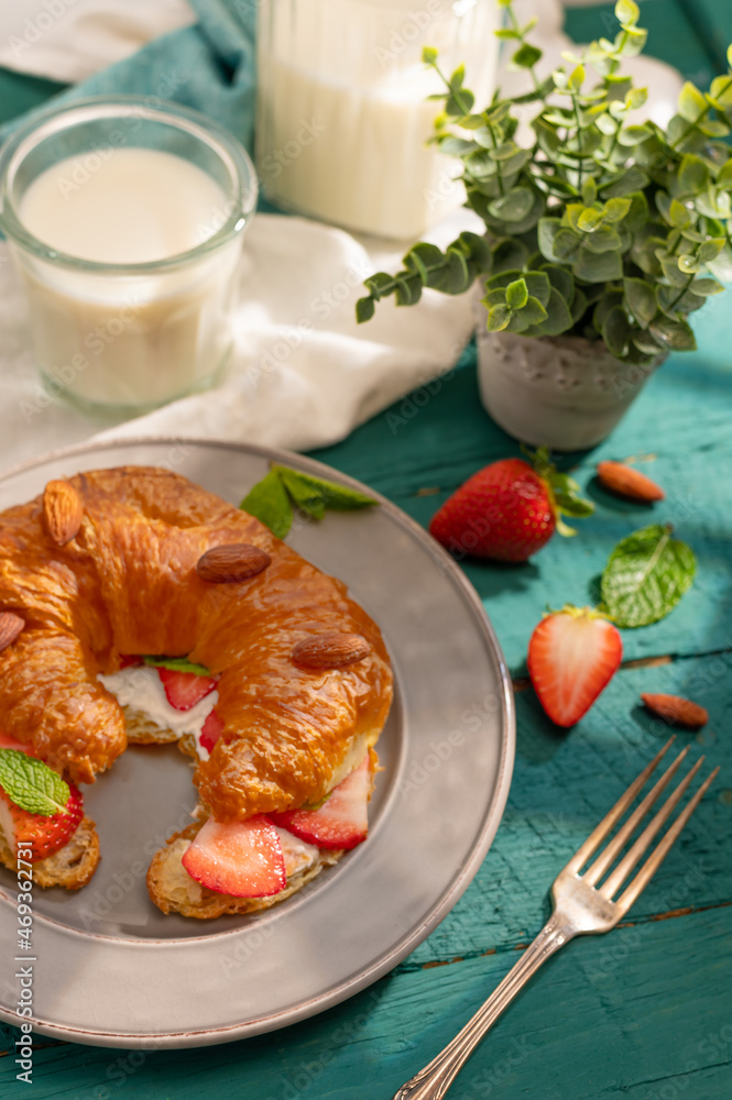 French breakfast for one person. On a plate, one croissant with strawberries, almonds, mint leaves, milk. Decor. Turquoise and white background. Culinary blog, instagram, restaurant, cafe, hotel. French breakfast for one person. On a plate, one croissant with strawberries, almonds, mint leaves, milk. Decor. Turquoise and white background. Culinary blog, instagram, restaurant, cafe, hotel.