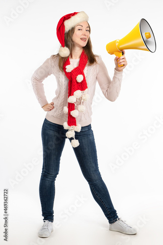 Call for Christmas sales concept. Woman in santa claus hat and scarf. Woman in Christmas accessories is advertising something. Advertising of New Year's shopping. Girl with loudspeaker on white
