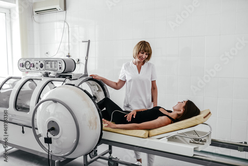 Young female doctor checking mask of a patient during hyperbaric oxygen therapy at clinic. photo