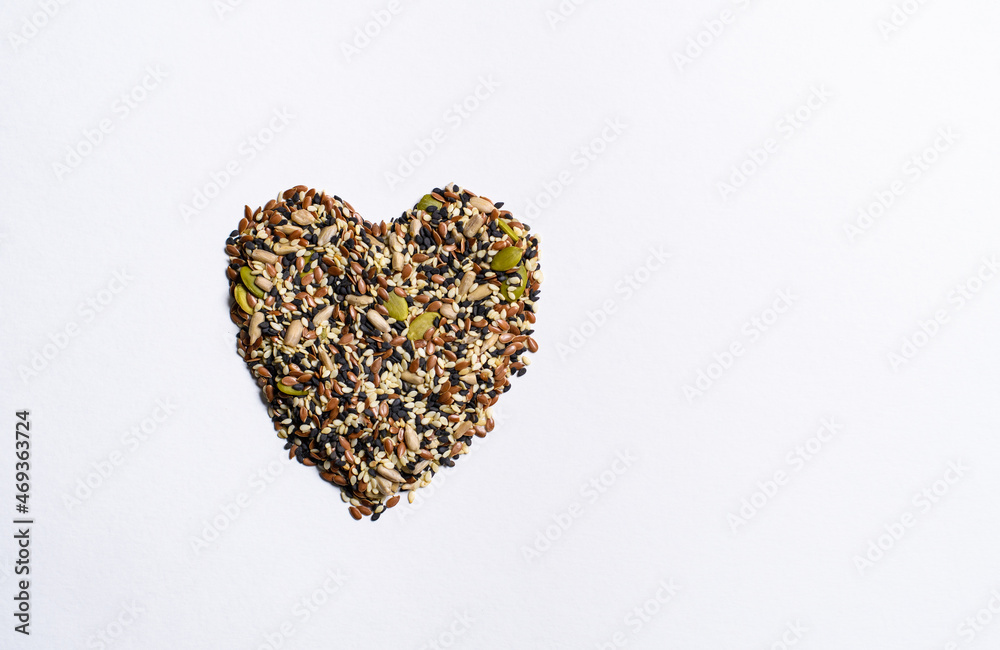 A mixture of different seeds in the shape of a heart lie on a white background. View from above