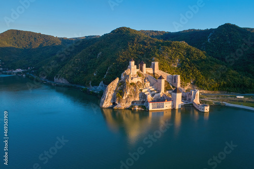 The medieval fortress of Golubac against iron gate of national park Djerdap, mirroring in the waters of the Danube. Colorful sunset light, blue sky. Aerial shot. Famous tourist place, Serbia. photo