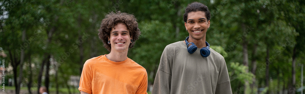young and happy interracial men looking at camera outdoors, banner.