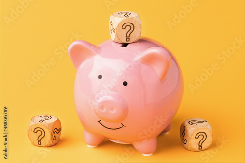 Wooden cubes with a question mark near a piggy bank on a colored background, the concept of choosing a currency to store money