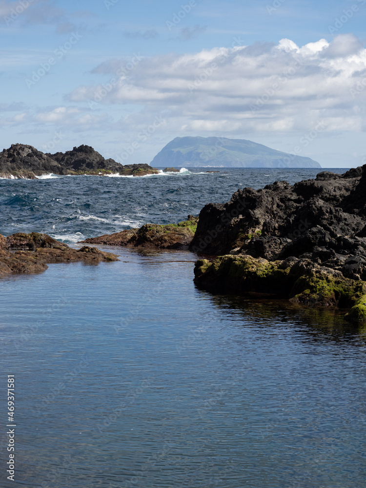 Amazing view with the contrast between rough and calm waters in the natural pools of Santa Cruz das Flores, of volcanic origin. In the background the remote island of Corvo. Flores Island.