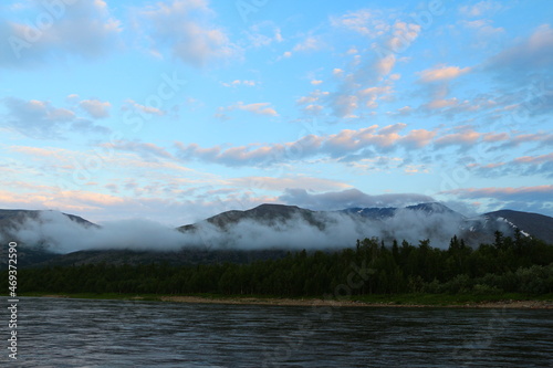 Heavenly landscape in the morning at dawn with white clouds illuminated by the sun in the blue sky with fog in the mountains spreading over the forest and the lake