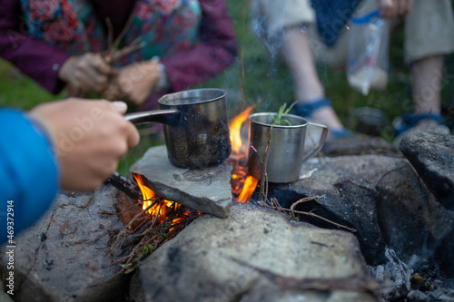 people on a hike make tea over a fire in a metal mug