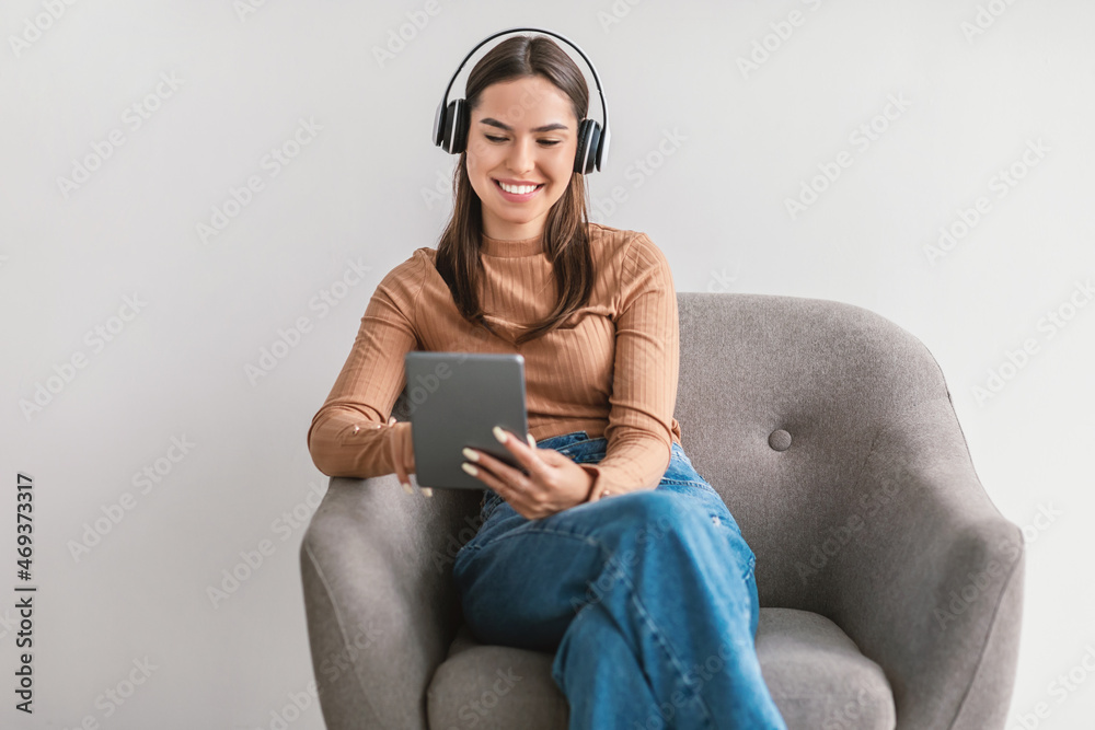 Happy Caucasian woman having video call, using tablet pc, sitting in armchair with headphones against white background Happy Caucasian woman having video call, using tablet pc, sitting in armchair with headphones against white background