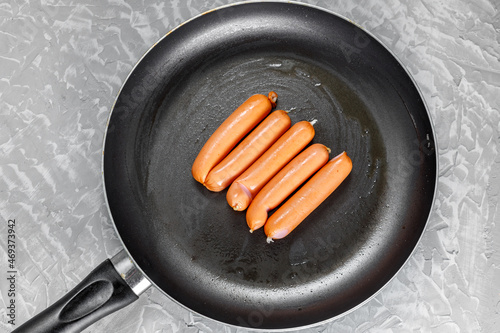 Beef sausages lie in a frying pan with a non-stick coating, greased with oil. Cooking at home.