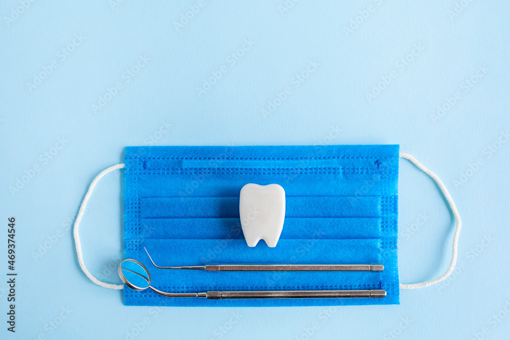 set of dental instruments, equipment, mirror and probe, toy tooth, medical mask on blue background. dental treatment, concept. copy space for text set of dental instruments, equipment, mirror and probe, toy tooth, medical mask on blue background. dental treatment, concept. copy space for text