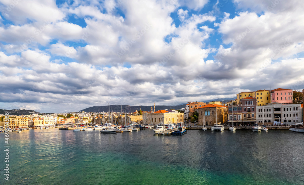 A panorama of the seaport town Chania, the island of Crete, Greece. A harbor with wooden pantons, moored yachts, ships, boats. Colorful architecture of modern and old houses. Mountains on the horizon