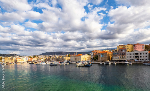 A panorama of the seaport town Chania, the island of Crete, Greece. A harbor with wooden pantons, moored yachts, ships, boats. Colorful architecture of modern and old houses. Mountains on the horizon © Vitalii_Mamchuk