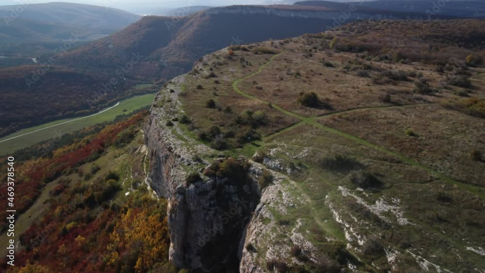 Flying over the cliff in the Mangup gorge. The edge of the white cliff rises above the bright trees. Bright colors of the Crimean autumn. 4k drone video Flying over the cliff in the Mangup gorge. The edge of the white cliff rises above the bright trees. Bright colors of the Crimean autumn. 4k drone video