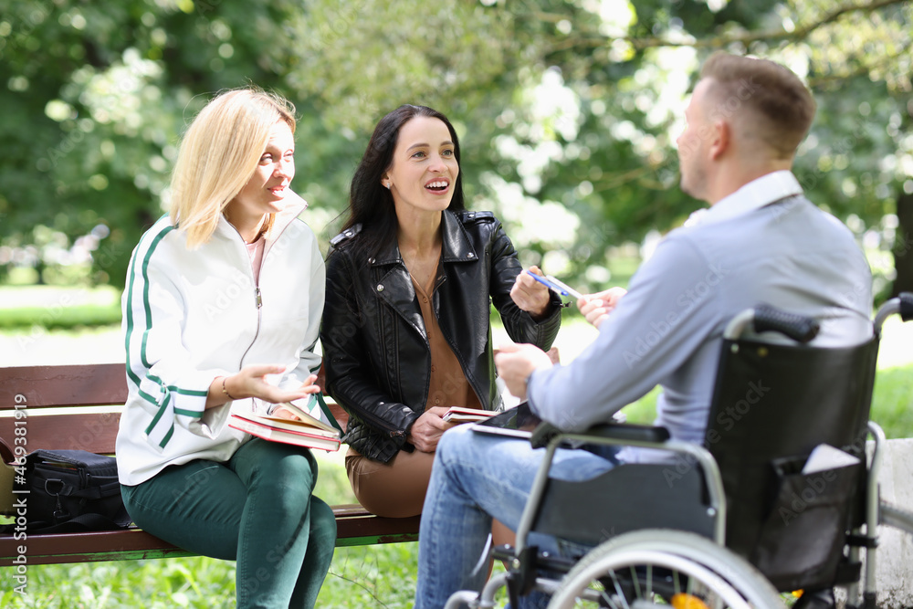 Two young women communicate with a man in wheelchair in park