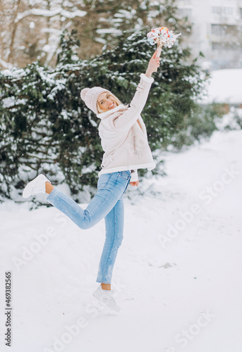 Cheerful woman with blond hair holding a bouquet of dried flowers and circling in a winter park.