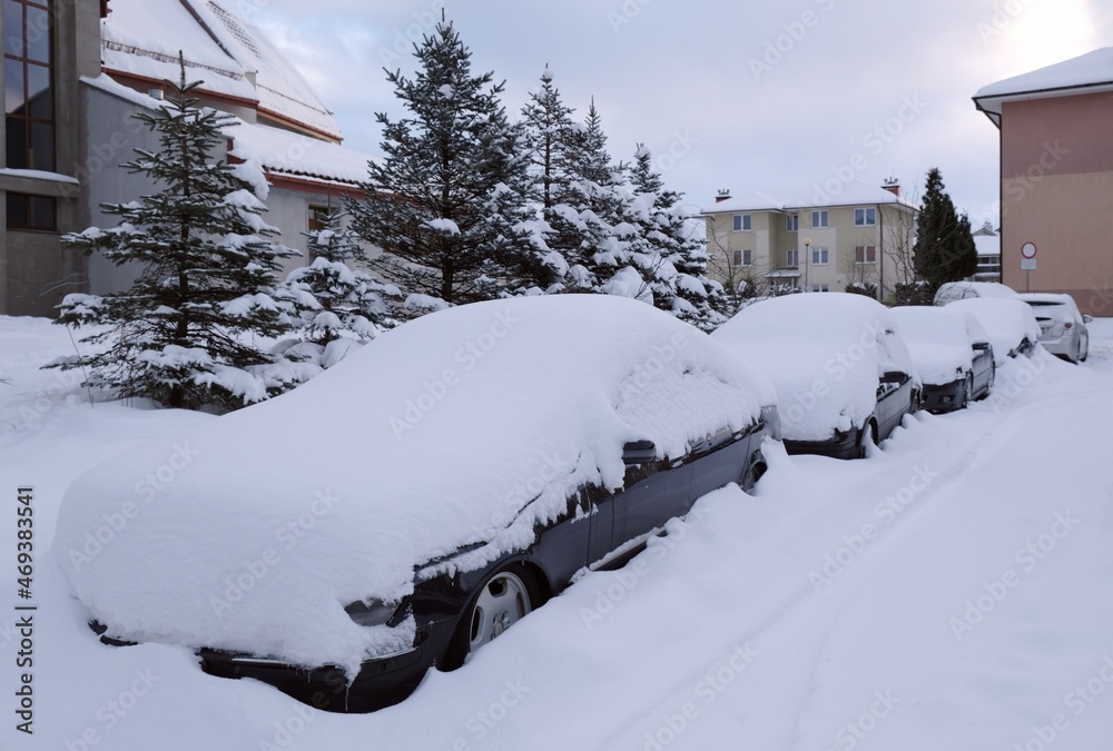 Fototapeta premium Cars covered with snow after snowstorm are standing in the street in town