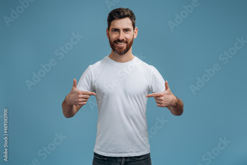 This is me. Portrait of happy man in T-shirt joyfully looking at camera and pointing to himself, proud of own success, egoistic person. Indoor studio shot isolated on blue background