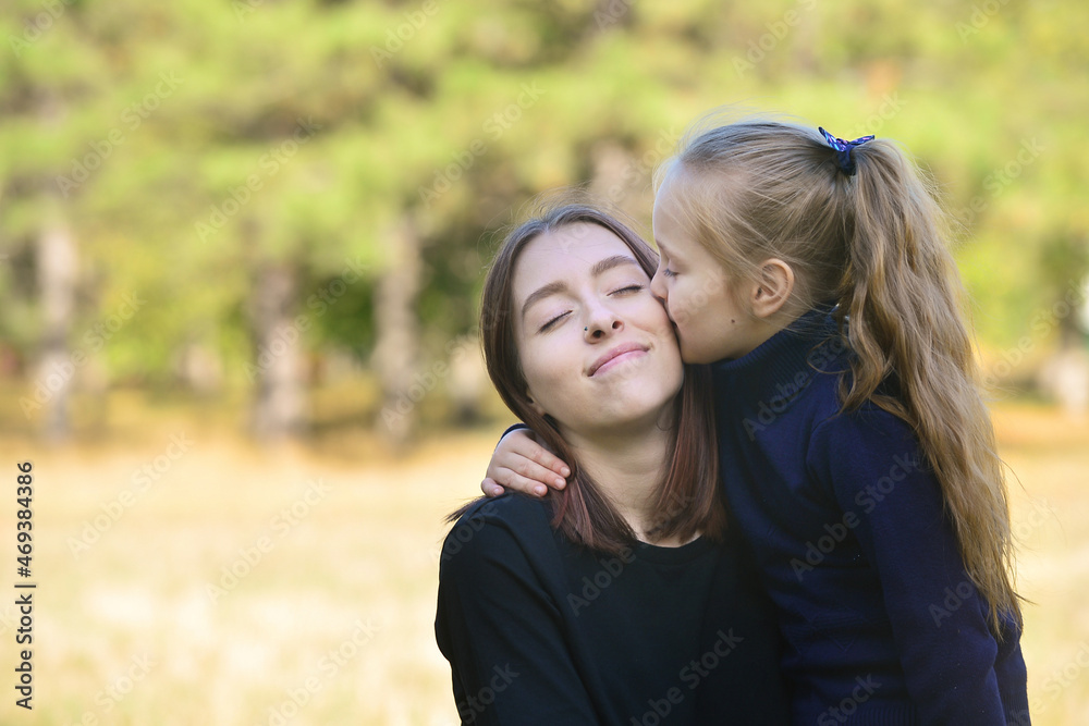 Two sisters, the youngest and the oldest, hug in the park during the warm season. Love and understanding in the family, family values, trusting relationships Two sisters, the youngest and the oldest, hug in the park during the warm season. Love and understanding in the family, family values, trusting relationships