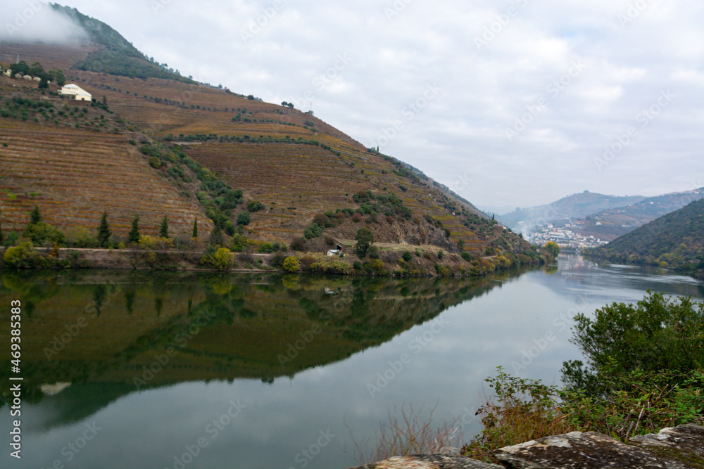 View on Douro river with reflection in water of colorful hilly stair step terraced vineyards in autumn, wine making industry in Portugal View on Douro river with reflection in water of colorful hilly stair step terraced vineyards in autumn, wine making industry in Portugal