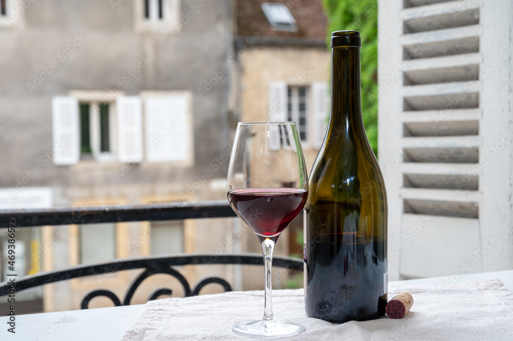 Tasting of burgundy red wine from grand cru pinot noir  vineyards, glass and bottle of wine and view on old town street in Burgundy wine region, France
