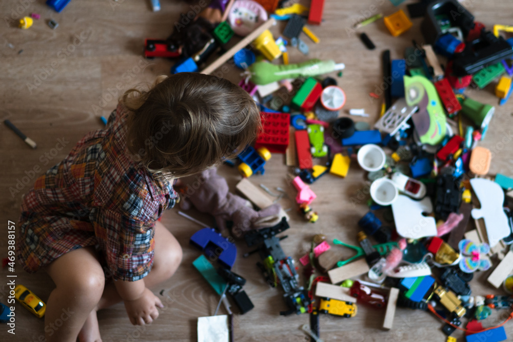 Fototapeta premium Mess in the nursery.Baby plays while sitting on the floor in colorful blocks. Homeschooling concept 