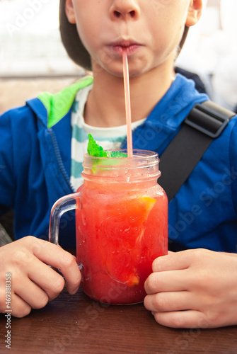 Summer refreshing fruit cocktail with a straw in the hands of a teenager. A child drinks lemonade in a cafe.