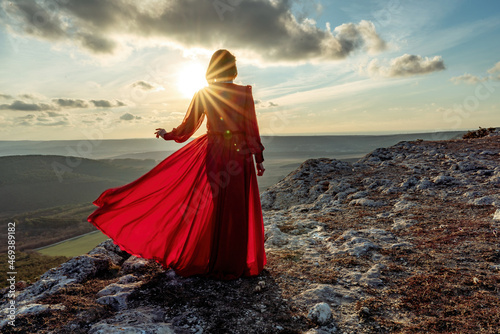 Rise of the mystic. sunset over the clouds with a girl in a long red dress. Stands on the mountain with a magical view.