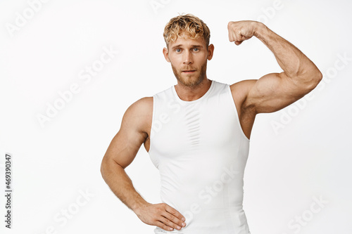 Portrait of strong and handsome young athlete showing his muscle on arm, flexing biceps and looking confident, white background
