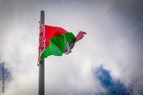 large state red-green flag of Belarus is flying in strong wind in cloudy sky photo