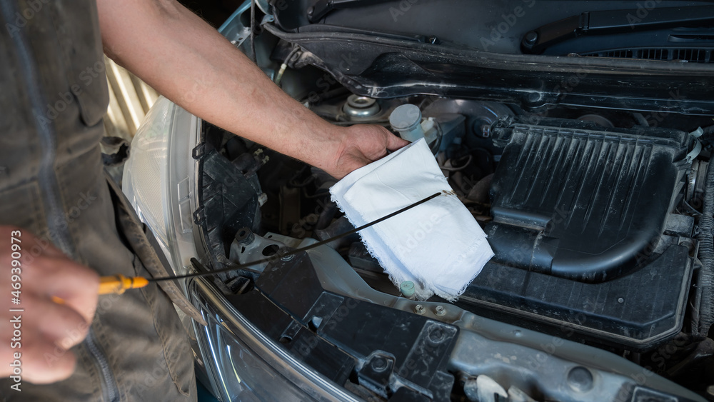 Auto mechanic wipes the dipstick to check the oil level in the engine. Auto mechanic wipes the dipstick to check the oil level in the engine.