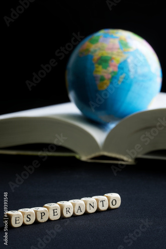 Esperanto inscription next to the globe and open book, dictionary. The concept of creating, learning and using the Esperanto language. Dark background. Macro. Selective focusing photo