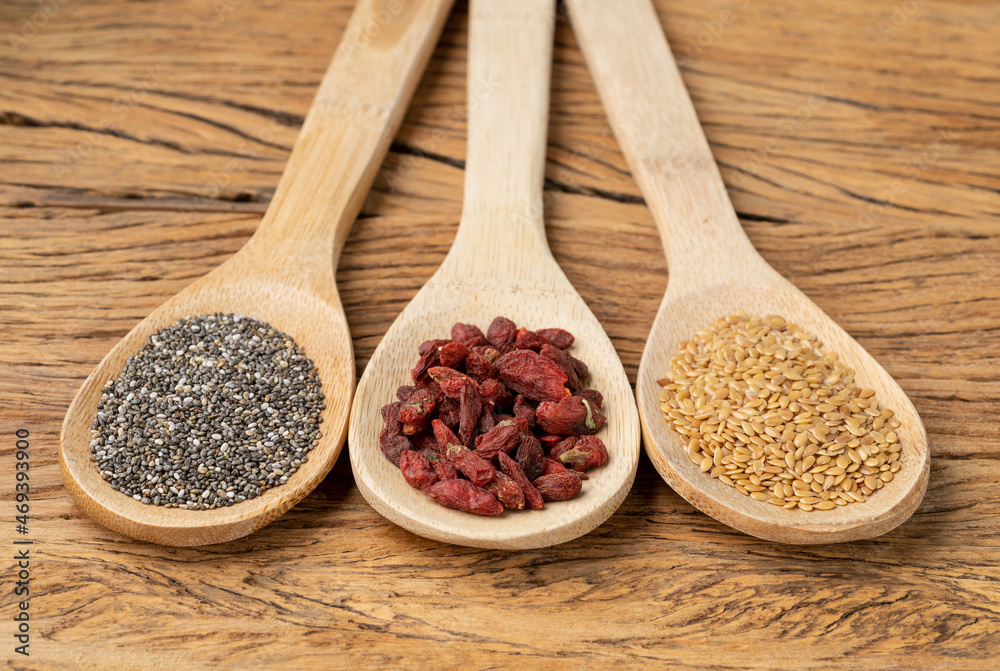 Assorted superfoods in spoons over wooden table. Chia, linseed and goji berry Assorted superfoods in spoons over wooden table. Chia, linseed and goji berry