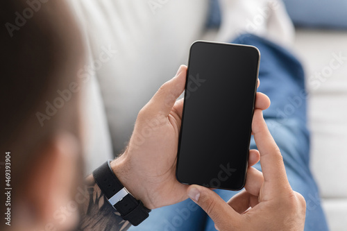 Cropped adult caucasian guy look at phone with blank screen  mockup  surfing in internet  sit on sofa  rest at free time