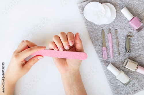 Female hands with white manicure next to cosmetic products for nail care