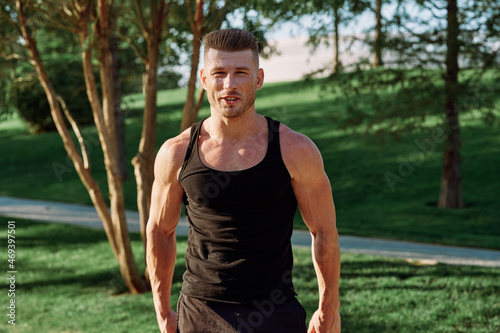 athletic man in black t-shirt with dumbbells in the park training
