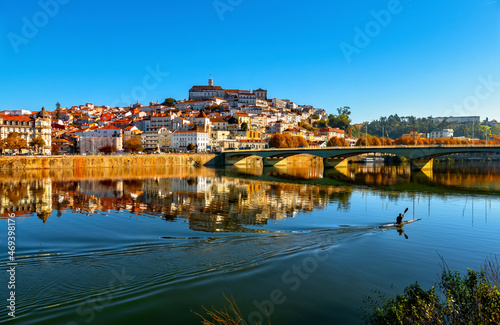 Canoísta a navegar em kayak no Rio Mondego e cidade de Coimbra com o reflexo na Água. Universidade de Coimbra e Ponte de Santa Clara.