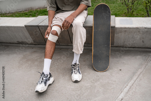 Photography cropped view of african american man bandaging injured knee near skateboard