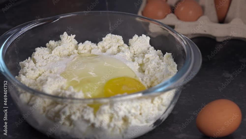 Breaking egg and pouring egg inside bowl with curd cheese dough, home cooking dough for cottage cheese pancakes Breaking egg and pouring egg inside bowl with curd cheese dough, home cooking dough for cottage cheese pancakes