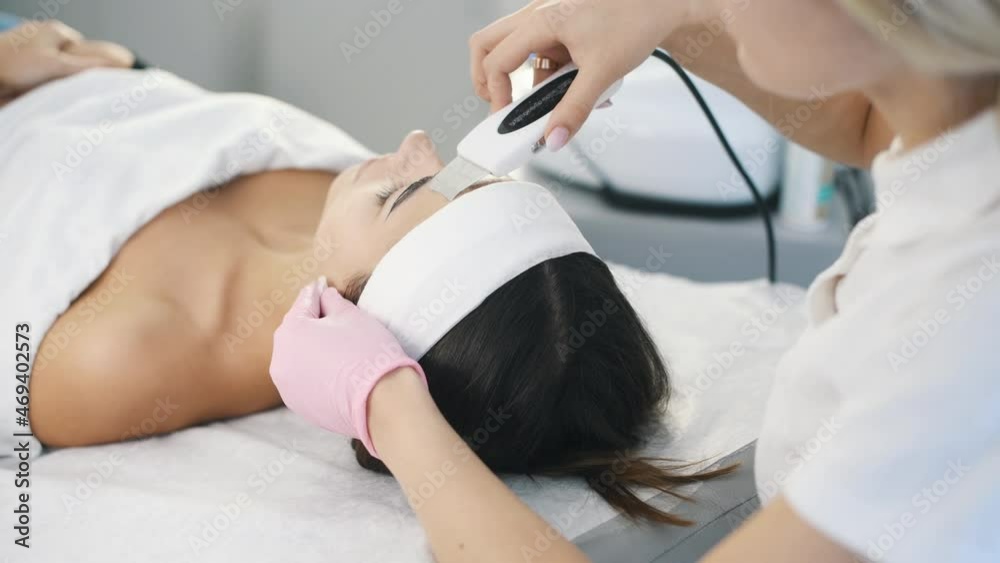 Close up view of woman that lying down in spa salon and have face cleaning procedure by using special modern device Close up view of woman that lying down in spa salon and have face cleaning procedure by using special modern device