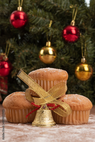 details of delicious cupcakes with a bell decorating, on a wooden table in the background a christmas tree, delicious sweet food in studio, baked dessert