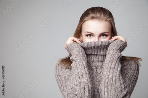 Beautiful blond young girl wears winter pullover over gray background