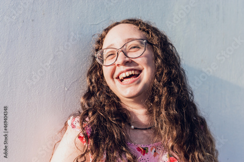 portrait of young hispanic latina girl with curls leaning against a wall smiling happily