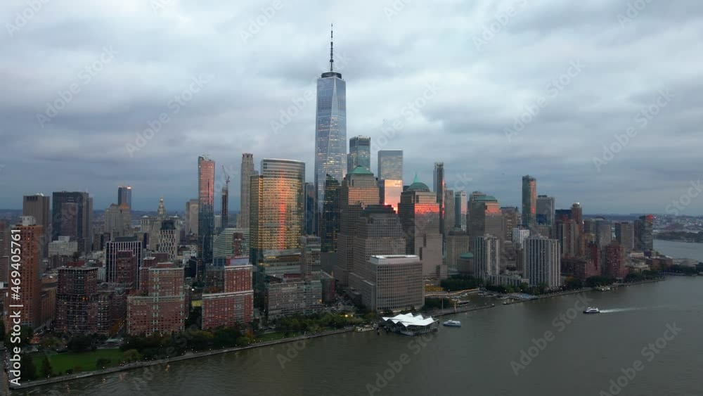 Aerial drone view towards sunlit skyscrapers in lower Manhattan, dark, cloudy sunset in New York, USA