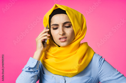 muslim woman in yellow hijab talking on the phone pink technology background © VICHIZH