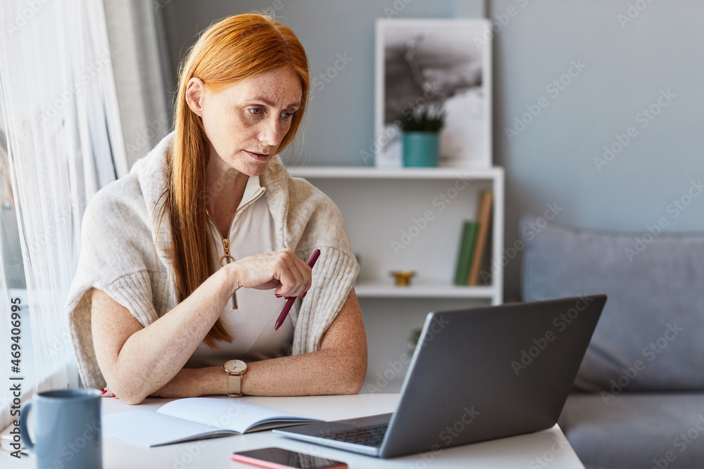Portrait of adult red haired woman using laptop while working at home office, copy space Portrait of adult red haired woman using laptop while working at home office, copy space