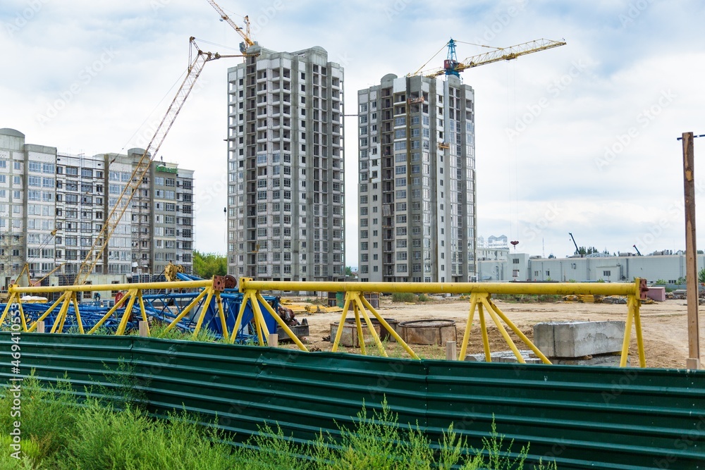 Large construction site including several cranes working on a building complex, with clear blue sky and the sun Large construction site including several cranes working on a building complex, with clear blue sky and the sun