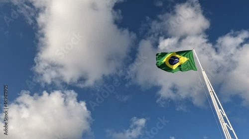 Huge flag of brazil waving freely under a sky with some white clouds.