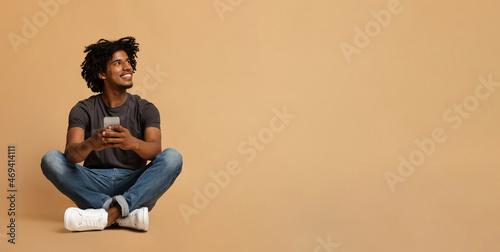 Mobile Offer. Smiling black man with smartphone in hands sitting on floor © Prostock-studio