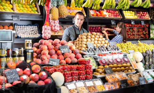 Friendly cheerful man and woman laying out vegetables and fruits in shop photo
