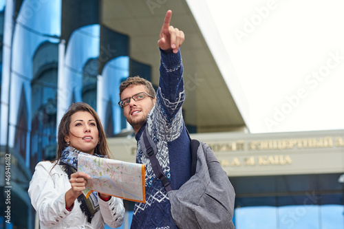 two happy tourists couple searching location together with a phone and map and pointing with the finger. Or female tourist asking for directions and help