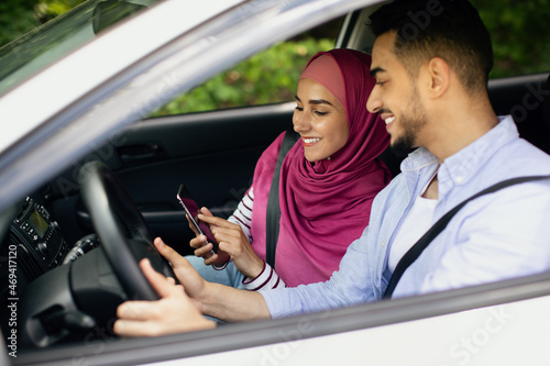 Young Muslim Spouses Riding Car And Using Smartphone Together, Through Window Shot